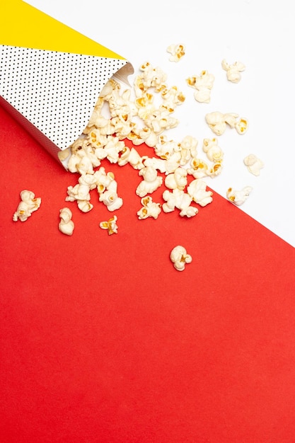 Концепция закуски Сладкий попкорн высыпается из бумажного стаканчика на красном и белом фоне