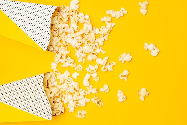 Концепция закуски Сладкий попкорн высыпается из двух бумажных стаканчиков на желтом фоне
