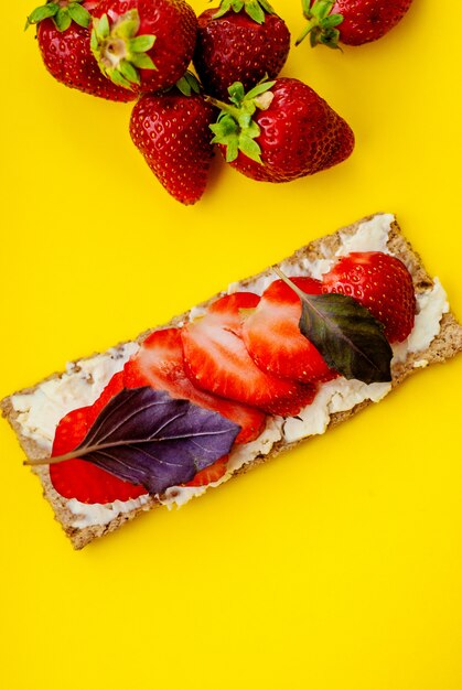 Snack met knäckebröd, roomkaas, verse aardbeien en basilicum op een gele achtergrond