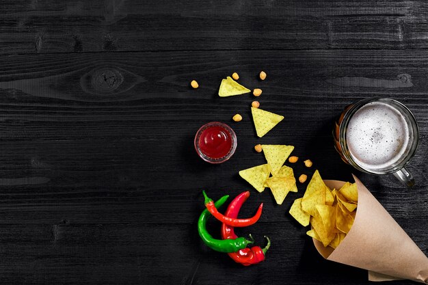 Snack for party chips nachos with sauces and mug of beer on a black background top view copy space