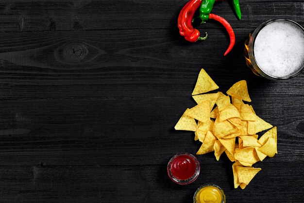 Snack for party chips nachos with sauces tomato ketchup  mustard and mug of beer on a black backgrou...
