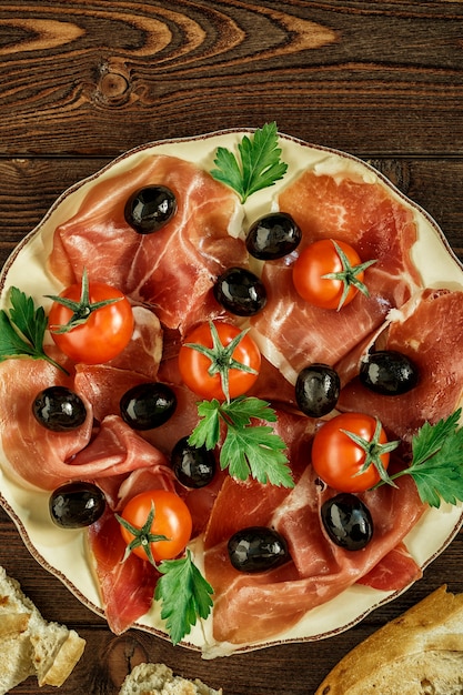 Snack plate of ham with olives and tomatoes