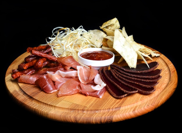 Snack tot bier op een houten bord. Basturma, gedroogd vlees, gedroogde inktvis, chips geïsoleerd op een zwarte achtergrond.