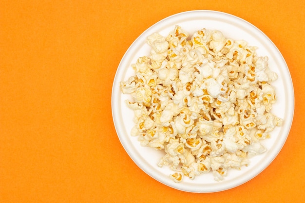 Snack of watching movie concept Sweet popcorn in white plate on orange background