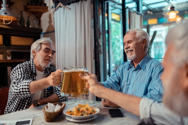 Snacks and beer. Retired grey-haired men feeling relieved while eating snacks and drinking beer