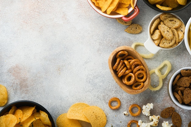 Snacks unhealthy food all classic potato snacks with peanuts\
popcorn and onion rings and salted pretzels in bowl plates on gray\
concrete background unhealthy food for figure heart skin teeth