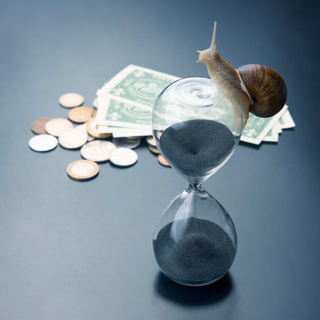 Snail crawls on an hourglass against the background of money