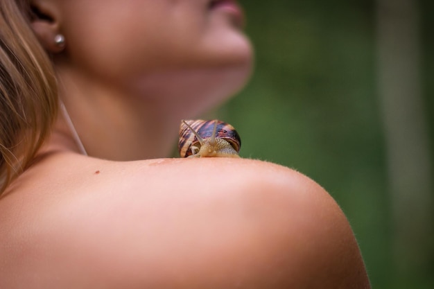 Snail sits on shoulder of caucasian woman Closeup of skin mollusk is visible