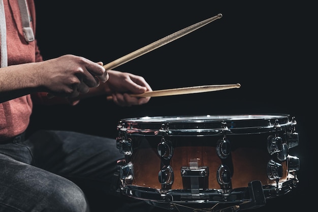 Snare drum and drummers hands hitting drumsticks against a dark background