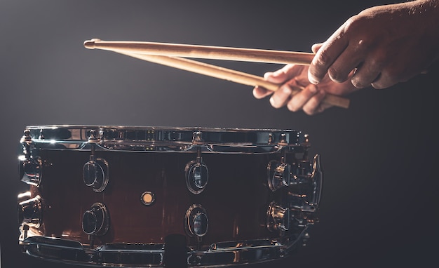 Snaredrum en drummer's handen raken drumsticks tegen een donkere achtergrond.