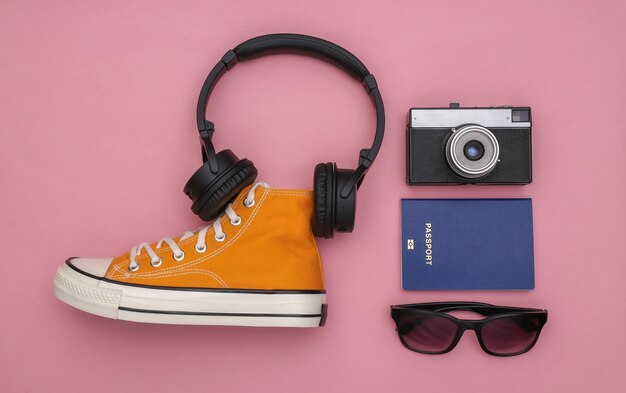 Sneaker and wireless stereo headphones, travel accessories on pink pastel background. Top view. Travel Flat lay