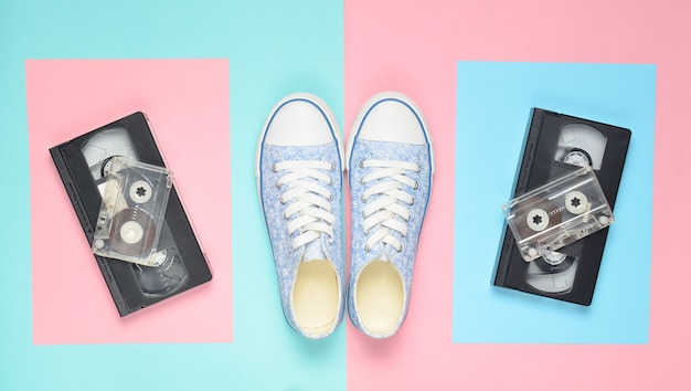 Sneakers, audio cassettes, video cassettes on a pink pastel blue surface. Retro attributes from the 80s. Top View