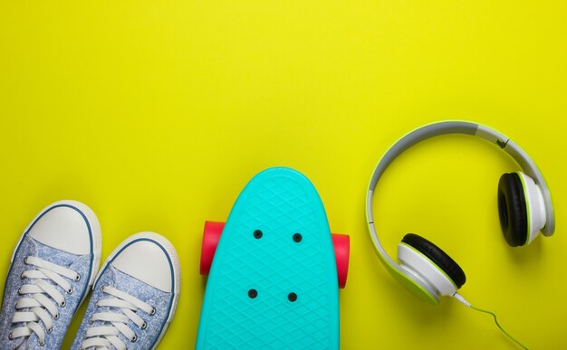 Sneakers, cruiser board and stereo headphones on green surface