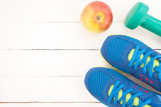 Sneakers, dumbbell fitness and apple on white wooden background