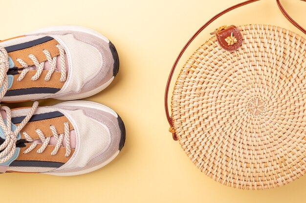 Sneakers en rotan tas op gele achtergrond. reis concept. plat leggen - afbeelding