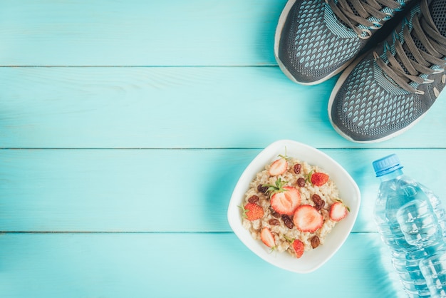 Sneakers, fles water, meetlint, havermout met aardbei en rozijnen en appel op blauw, plat leggen