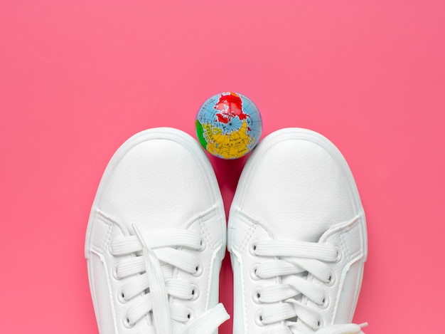 Sneakers and the globe on a pink background. Life style. Concept of travel. Top view. Flat lay.