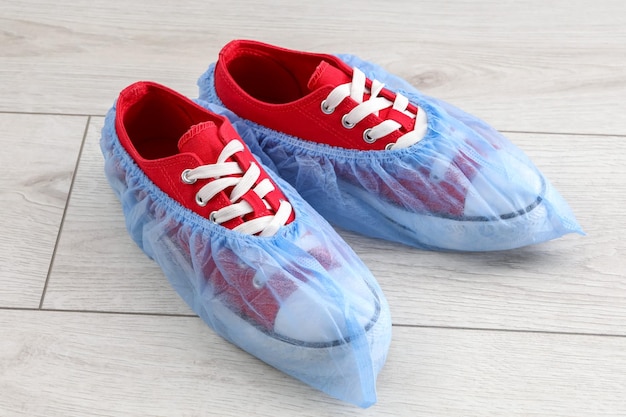 Sneakers in blauwe schoenbedekkingen op een lichte houten vloer