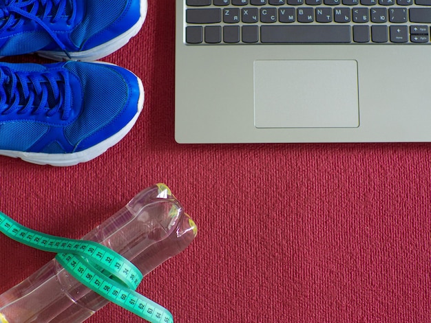 Sneakers laptop water bottle and measuring tape on a red yoga mat