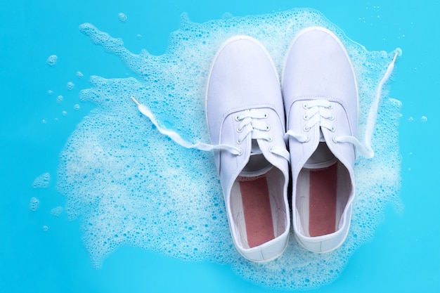 Sneakers met schuim van poeder wasmiddel water oplossen op blauwe achtergrond. Vuile schoenen wassen.