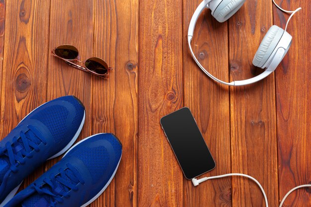 Sneakers and mobile phone with headphones on wooden table