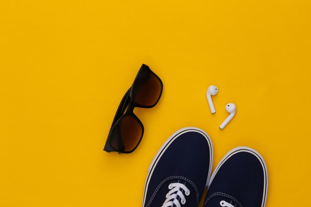 Sneakers shoes and wireless earphones, sunglasses on yellow background. 