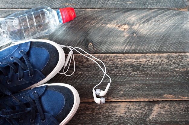 Sneakers, water and earphones on old wooden background