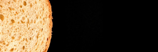 Sneetje wit brood close-up geïsoleerd op een zwarte achtergrond ruw getextureerde oppervlak gehakt stuk brood van natuurlijke biologische voeding met gaten bovenaanzicht abstract concept van de planeet en de ruimte banner