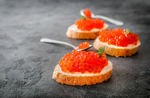 Sneetjes brood met rode kaviaar op donkere achtergrond.