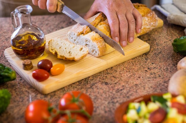 Sneetjes rustiek brood op de houten snijplank en twee vrouwenhanden die een snack bereiden met een tomatenbruschetta en pittige olie. Assortiment verse groenten op tafel