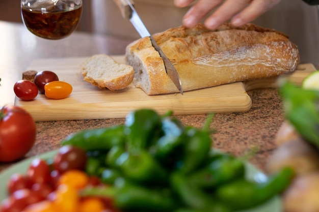 Sneetjes rustiek brood op de houten snijplank en twee vrouwenhanden die een snack bereiden met een tomatenbruschetta en pittige olie. Assortiment verse groenten op tafel