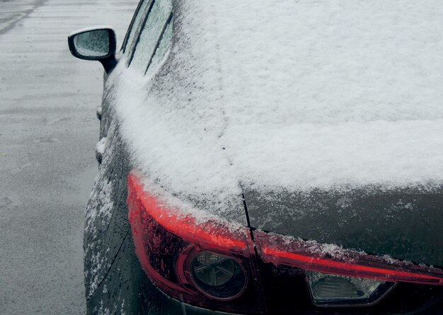 Sneeuw en ijs op het achterste deel van de auto op het natte asfalt