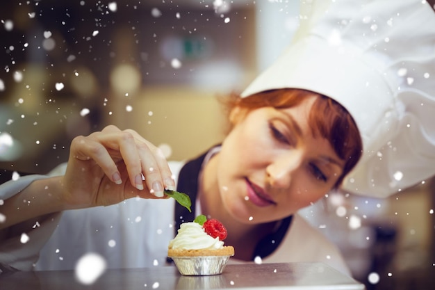 Sneeuw tegen gefocuste chef-kok die muntblad op kleine cake zet