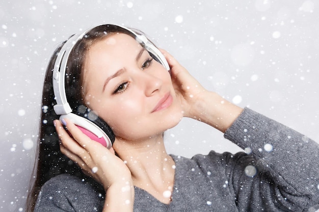 Sneeuw, winter, kerst, mensen, vrije tijd en technologie concept - gelukkige vrouw of tienermeisje in koptelefoon luisteren naar muziek van smartphone en dansen over sneeuw achtergrond