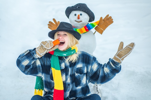 Sneeuwman met grappige wortelneussneeuwman en grappig vrouwelijk model in wintermuts en sjaal met...