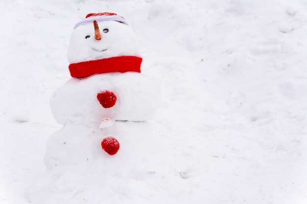 Sneeuwpop staande op de achtergrond van witte sneeuwbanken in het winterlandschap. Heel veel sneeuw. Sneeuwpop met een rode hoed, sjaal en knopen.