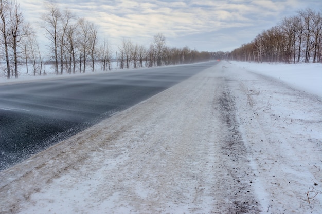 Sneeuwstorm op de snelweg. patronen op de wintersnelweg in de vorm van vier rechte lijnen. besneeuwde weg op de achtergrond van besneeuwd bos.