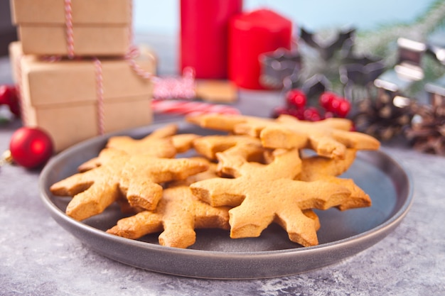 Sneeuwvlok vormige zelfgemaakte kerstkoekjes op de plaat met kerstversiering op de achtergrond.