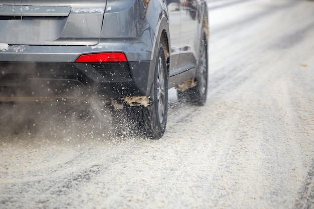 Sneeuwvlokken op de weg stromen van de wielen van een grijze auto die snel beweegt in de daglichtstad met selectieve focus