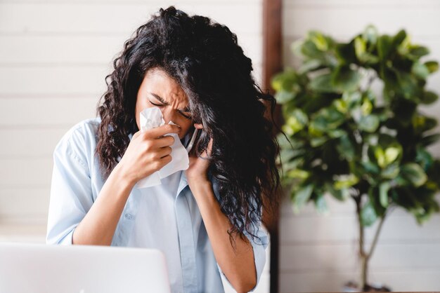 Sneezing sick with flu and cold young african businesswoman\
asking for sick leave on phone at work