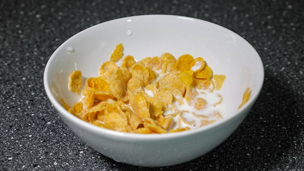 Snel ontbijt bereiden met ontbijtgranen. droge cornflakes en melk in kom met lepel.