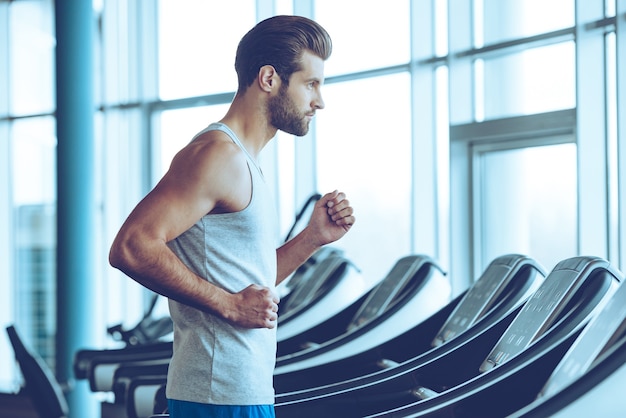 Snel rennen. Zijaanzicht van een jonge man in sportkleding die op de loopband in de sportschool draait