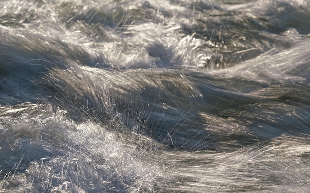 Snelle lente rivier die over rotsen stroomt op zonnige dag, wildwatergolven vormt, langere blootstelling ziet eruit als draden, close-up detail - abstracte natuur achtergrond