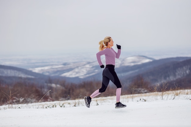 Snelle sportvrouw in vorm die snel loopt in de natuur op besneeuwde winterdag. Cardio-oefeningen, gezonde gewoontes, wintersport