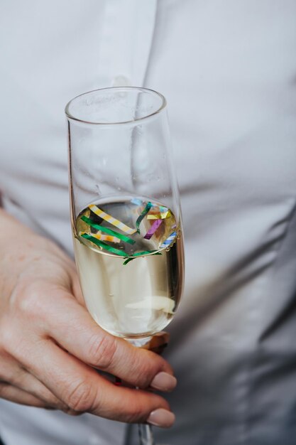 Snijd close-up vrouwelijke hand met glas champagne met kleurrijke confetti erin