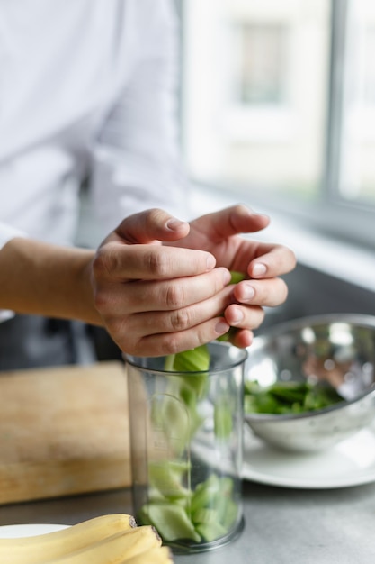 Snijd de handen van de mannelijke chef-kok die gesneden bleekselderij in de inhoud stopt voor het bereiden van verse smoothie