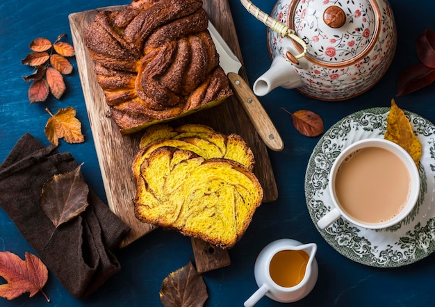 Snijd de pompoen brioche kaneel op rustieke houten snijplank thee met melk en een theepot op een blauwe achtergrond bovenaanzicht Heerlijke seizoensgebonden gebakjes