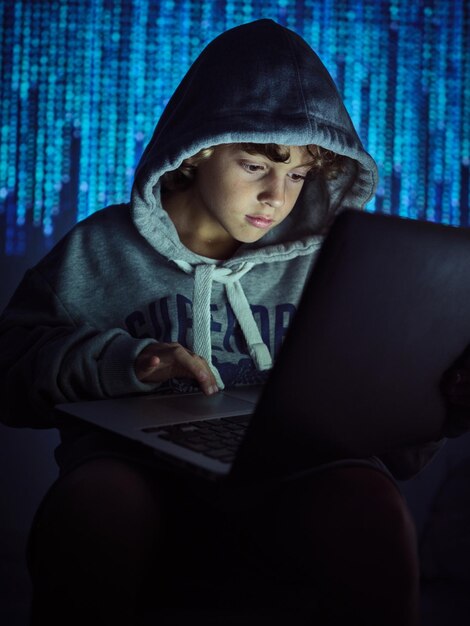 Snijd een jonge hacker bij die op een laptop typt terwijl cybercriminaliteit de achtergrond van de binaire code vervaagt bij weinig licht