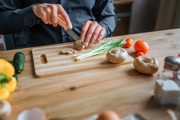 Snijd mening van man handen snijdend paddestoelen met mes. Hij werkt met beide handen. Mensentribune in keuken bij lijst.