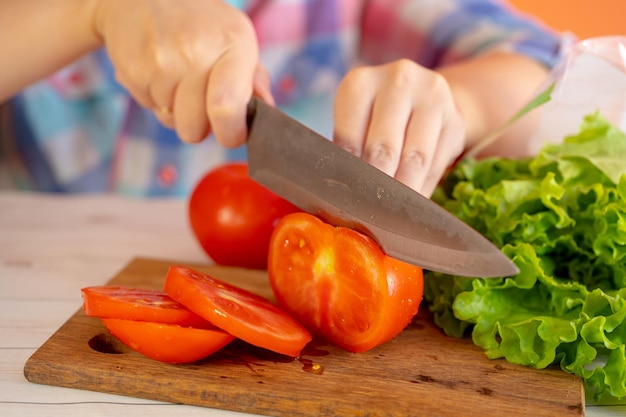 Snijd tomaten in halve rode tomaat op de snijplank in de keuken Vrouwelijke chef-kok snijdt een rode tomaat met een mes op houten snijplank het proces van koken close-up